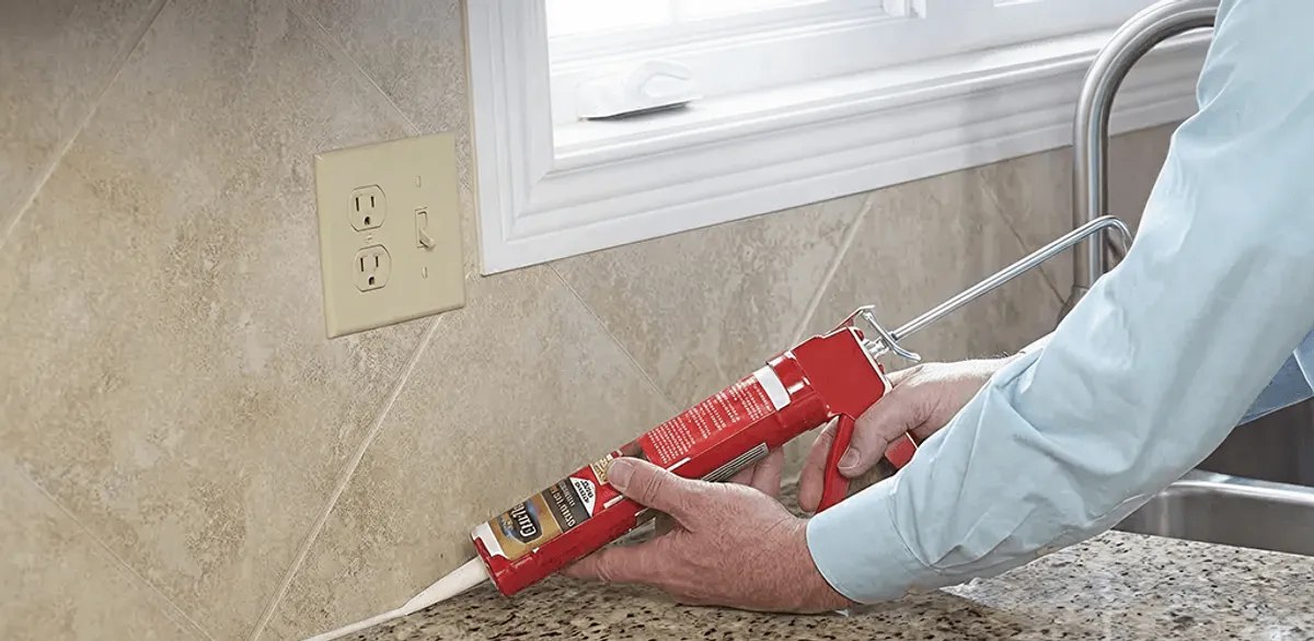 Handyman applying caulk along a kitchen backsplash and countertop seam in Mesa, AZ